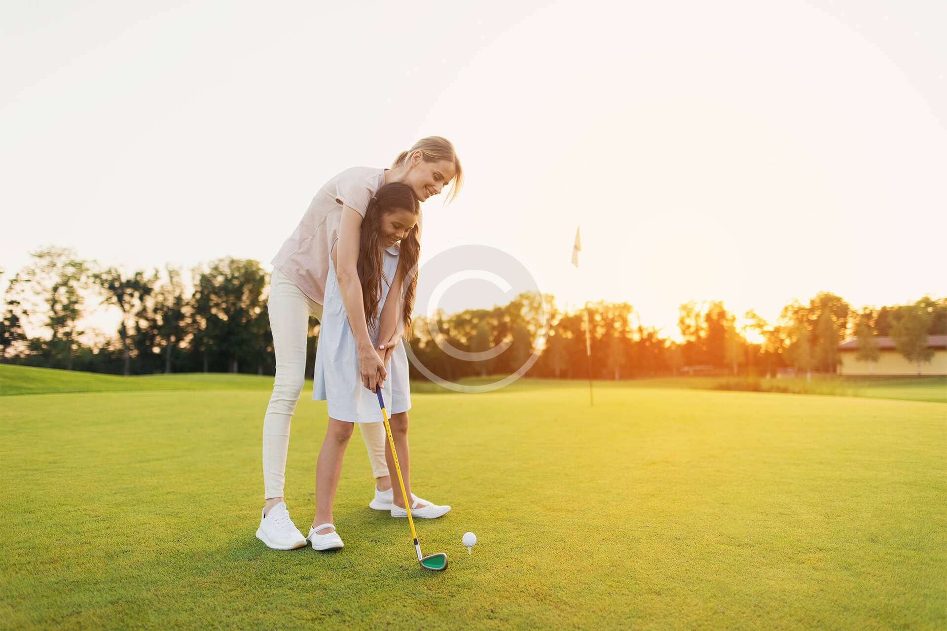 A girl teaching a child how to take a golfing shot on the course.