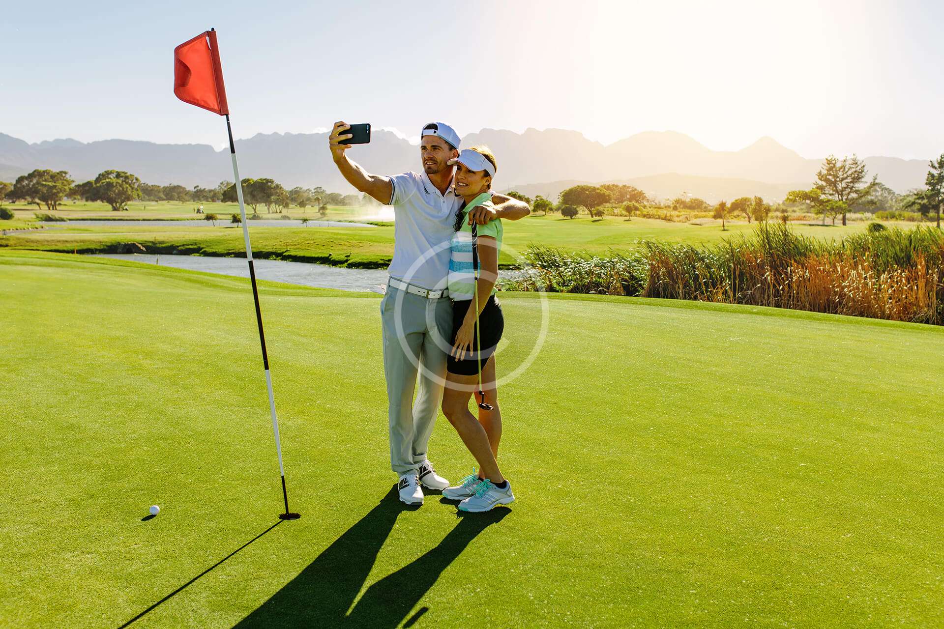 Boy and girl smiling together on a golf course, capturing a photo with golf clubs in hand.