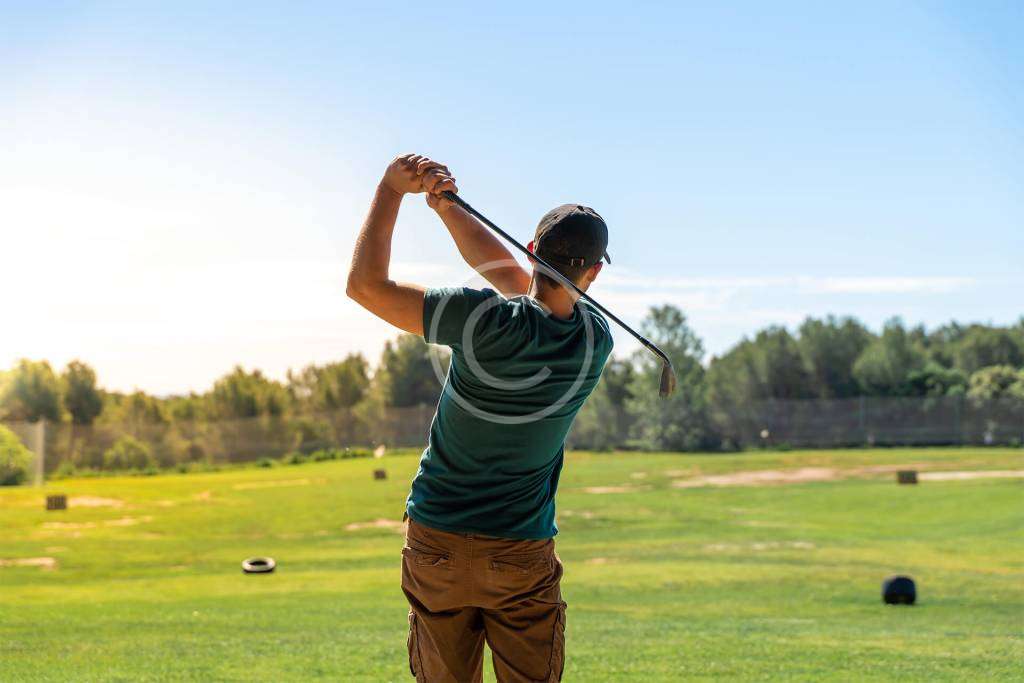 A man in a follow-through position after hitting a golf ball, with a copyright logo.