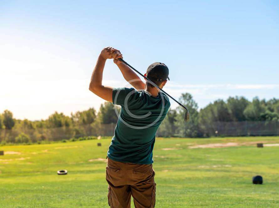 A man in a follow-through position after hitting a golf ball, with a copyright logo.