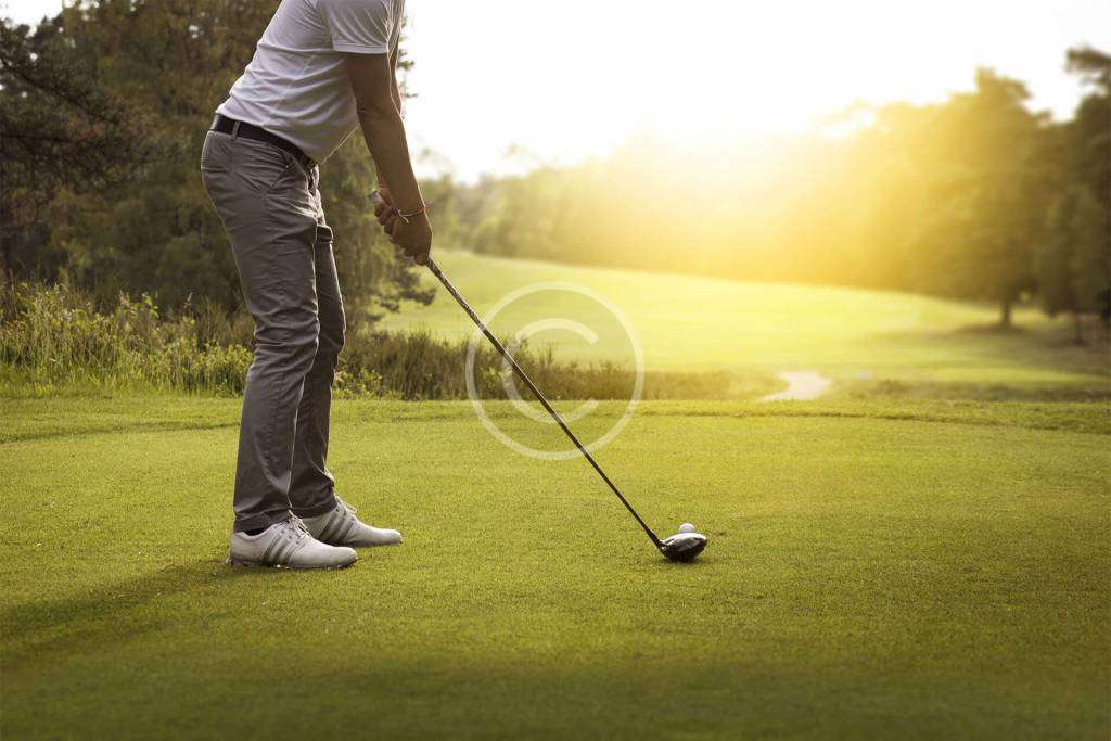 Male golfer in a set position, preparing to hit the ball with focus.