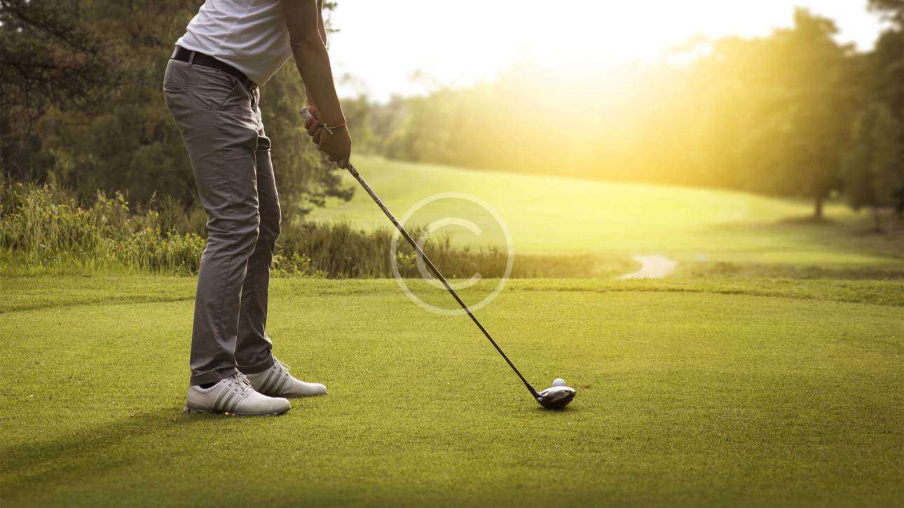 Male golfer in a set position, preparing to hit the ball with focus.