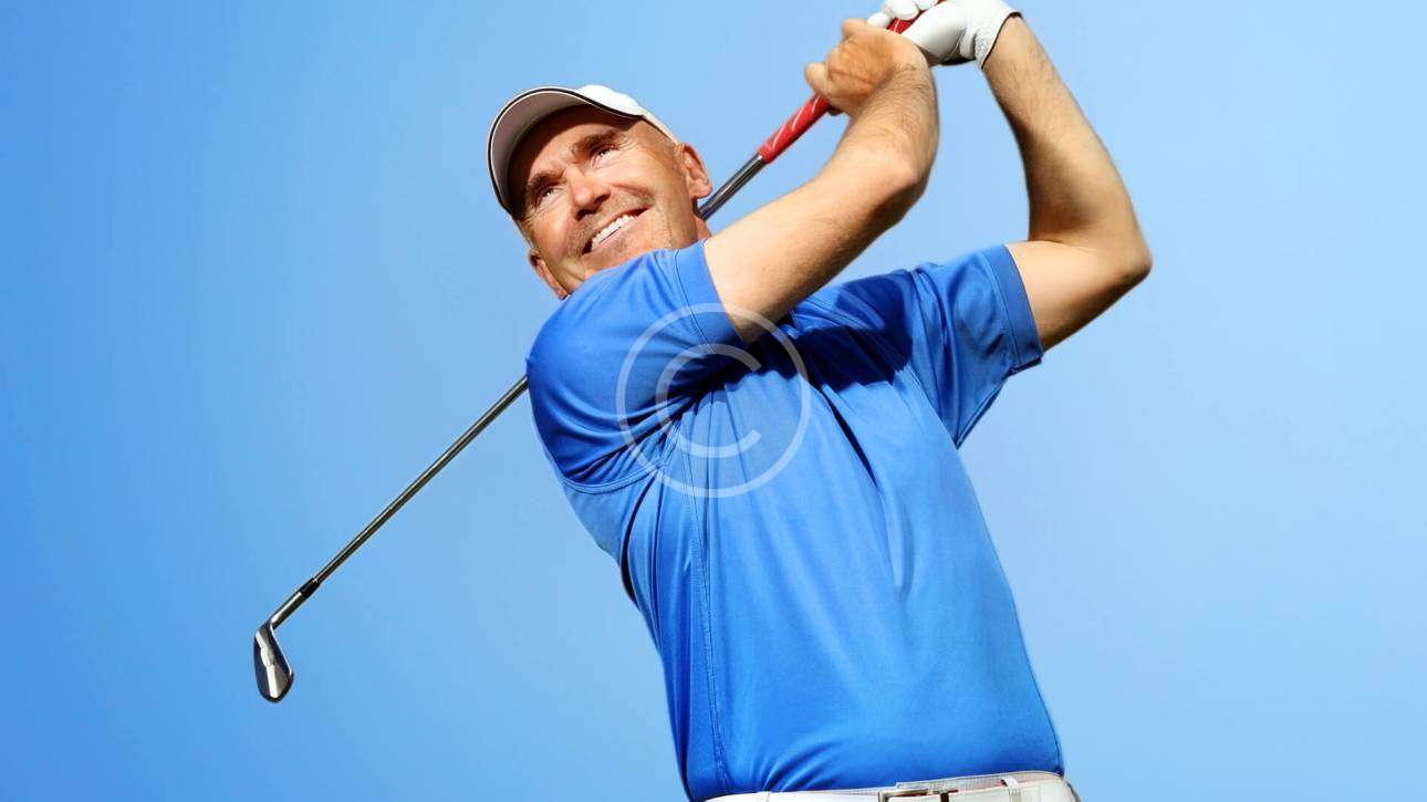 A man in a follow-through position with a golfing stick after hitting the ball, with a copyright logo.